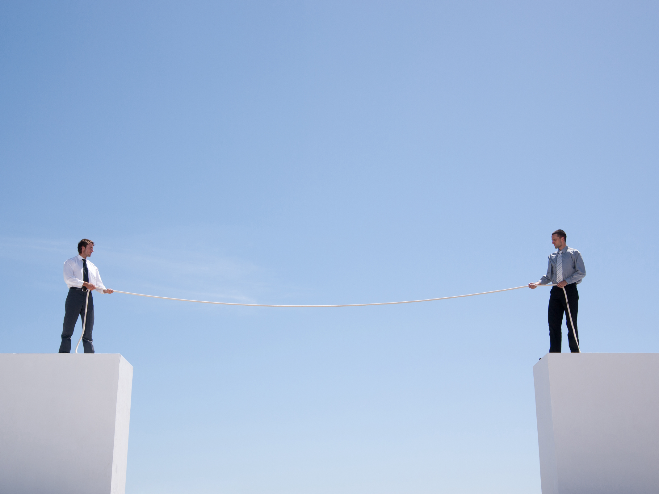 Businessmen standing on wall holding rope.